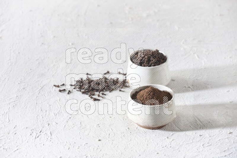 2 Beige ceramic bowls, one full of cloves and the other full of powder on textured white flooring