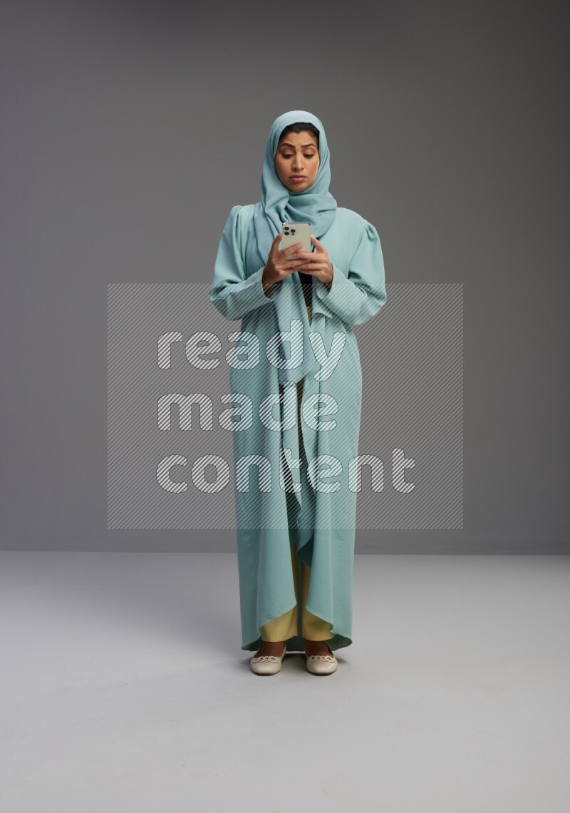 Saudi Woman wearing Abaya standing texting on phone on Gray background