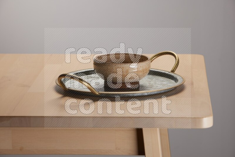 multicolored bowl placed on a rounded stainless steel tray with golden handels on the edge of wooden table