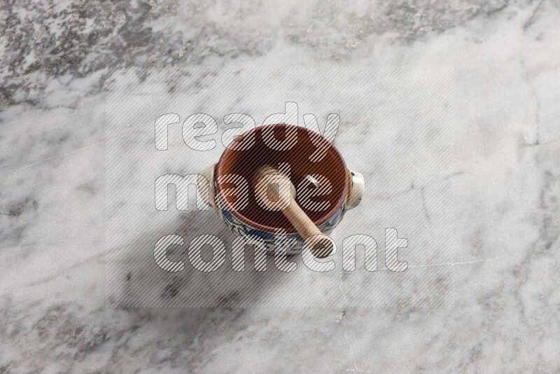 Decorative pottery pot with wooden honey dipper in it on grey marble background