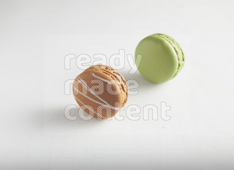 45º Shot of of two assorted Brown Irish Cream, and Green Pistachio macarons on white background