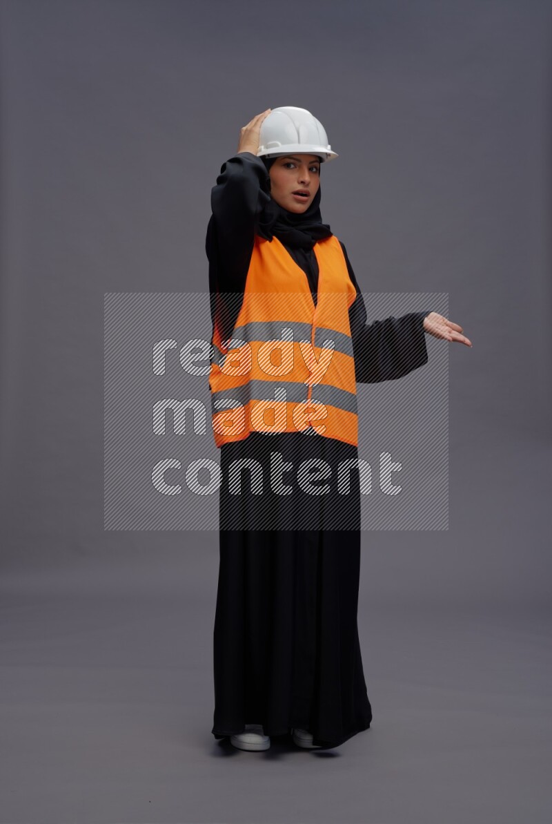 Saudi woman wearing Abaya with engineer vest standing interacting with the camera on gray background