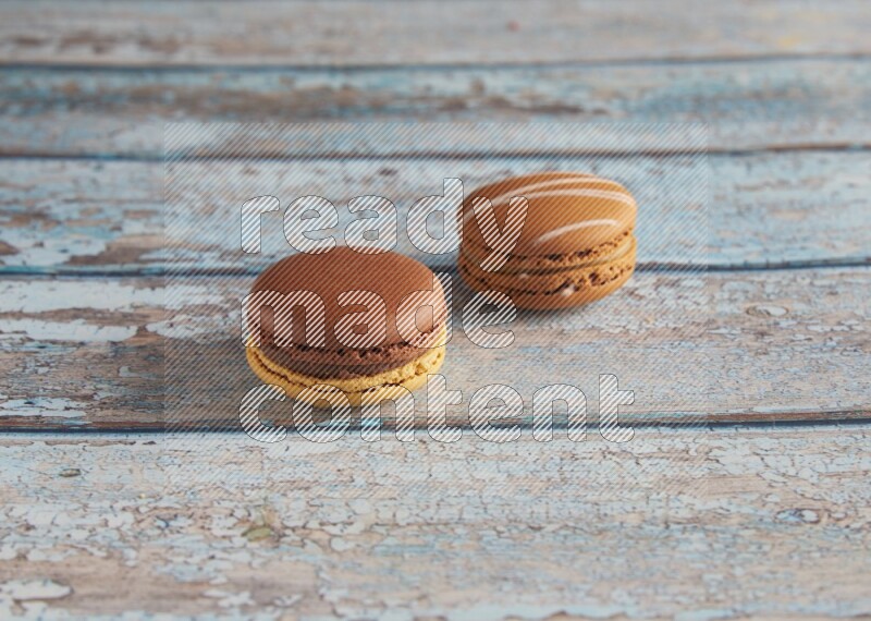 45º Shot of of two assorted Brown Irish Cream, and Yellow, and Brown Chai Latte macarons  on light blue background
