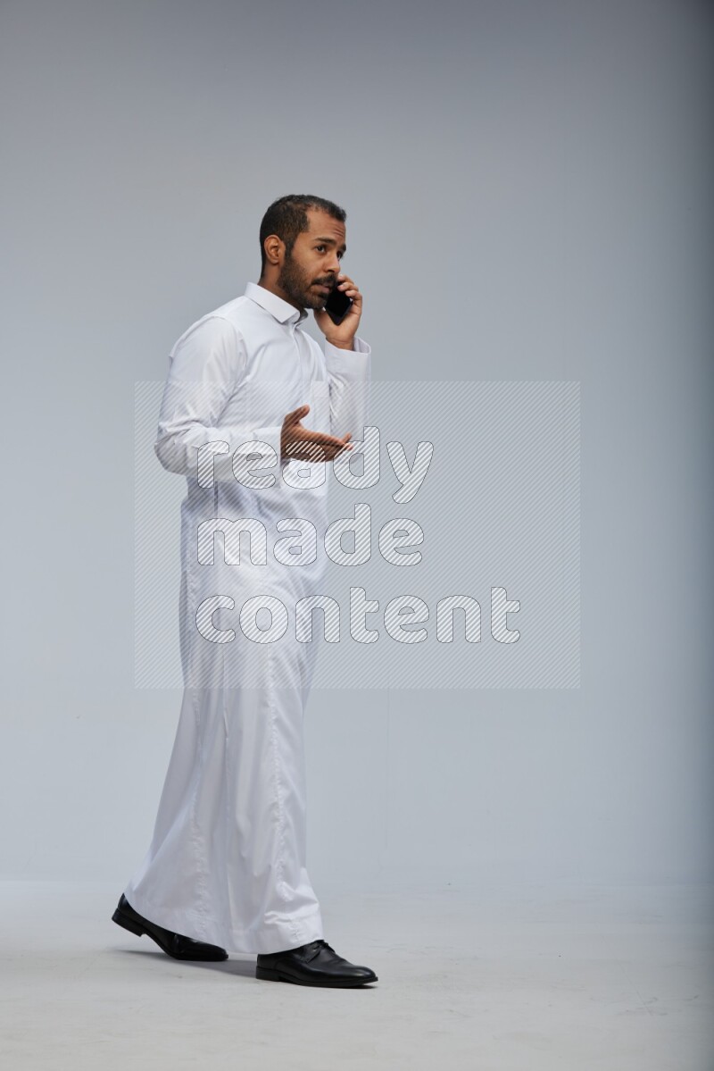 Saudi man wearing Thob standing talking on phone on Gray background