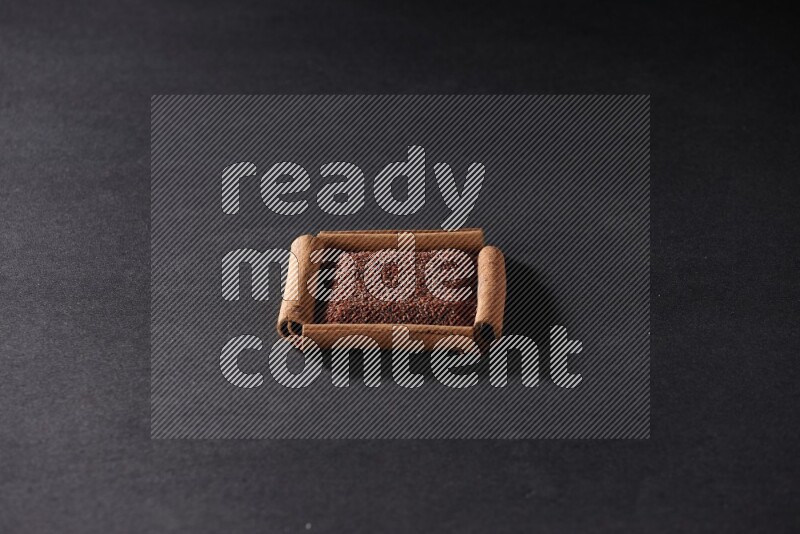 أربعة من أعواد القرفة مكونة شكل مربع بداخلها حب الرشاد علي خلفية سوداء