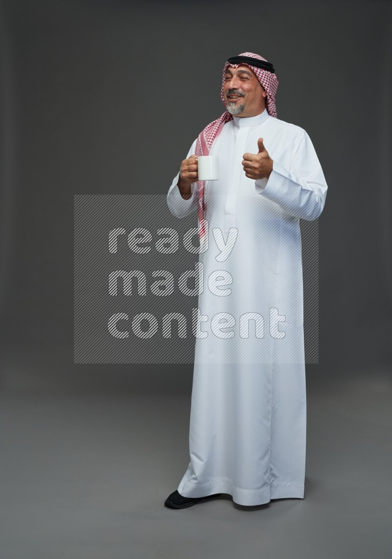 Saudi man with shomag Standing holding mug on gray background
