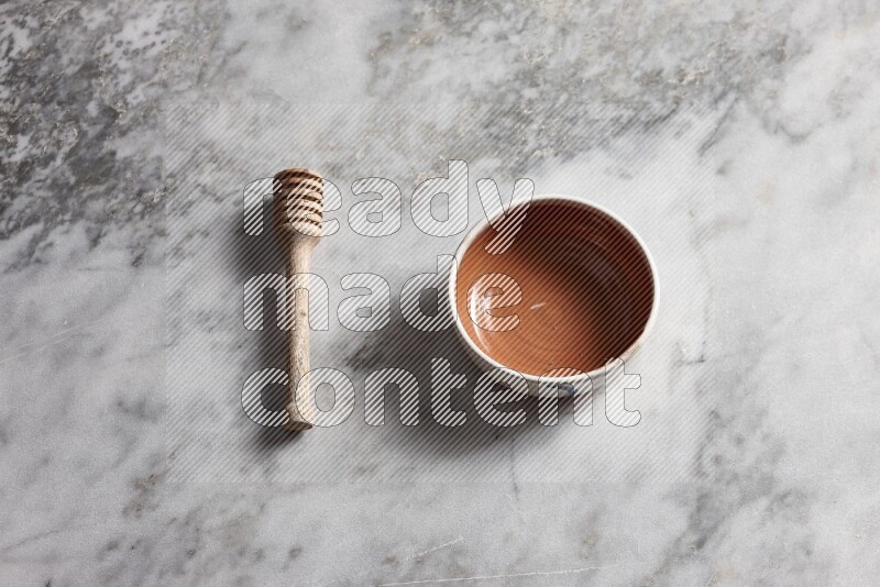 Multicolored pottery bowl with wooden honey dipper on the side on grey marble background