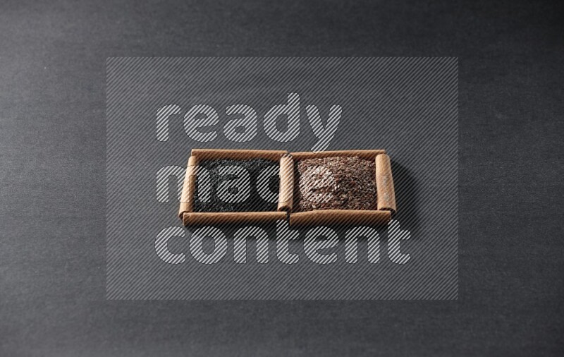 مربعان من أعواد القرفة ممتلئان ببذور الكتان وحبة البركة السوداء علي خلفية سوداء