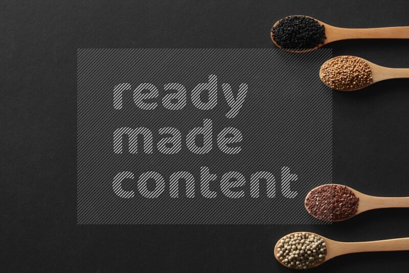 wooden spoons filled with white peppers, mustard seeds, black seeds, garden cress, cumin and flax on black flooring