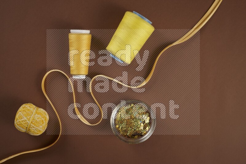A yellow collection of sewing and tailoring tools arranged on a brown background