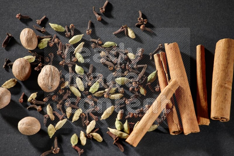Cardamom, cloves, nutmeg and cinnamon sticks on black flooring