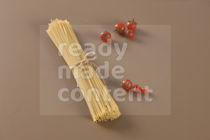 Raw pasta with different ingredients such as cherry tomatoes, garlic, onions, red chilis, black pepper, white pepper, bay laurel leaves, rosemary and cardamom on beige background