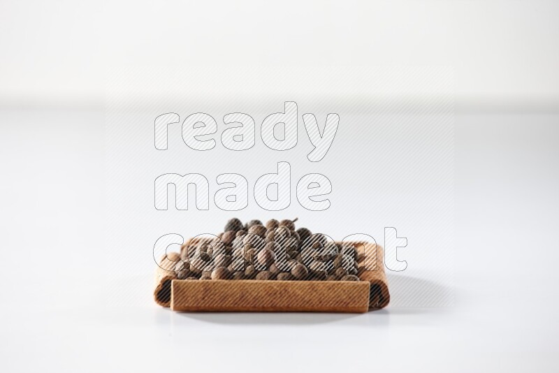 أربعة من أعواد القرفة مكونة شكل مربع بداخلها بهار الفلفل الحلو علي خلفية بيضاء