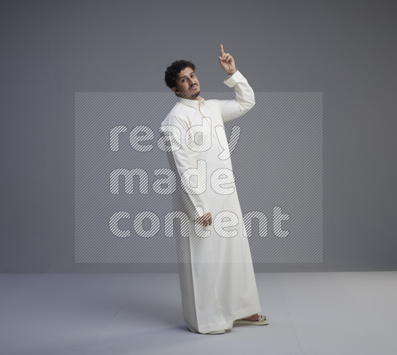 A Saudi man standing wearing thob interacting with the camera on gray background