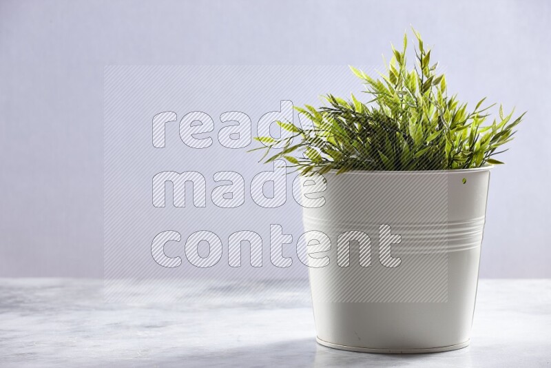 Green artificial plant in white pot on grey marble background