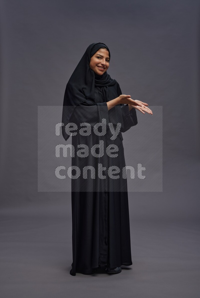 Saudi woman wearing Abaya standing interacting with the camera on gray background