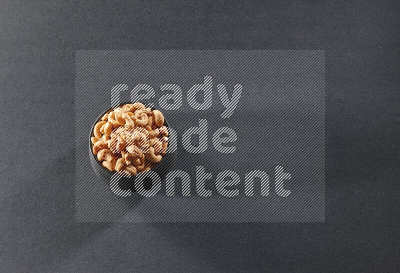 A black pottery bowl full of cashews on a black background in different angles