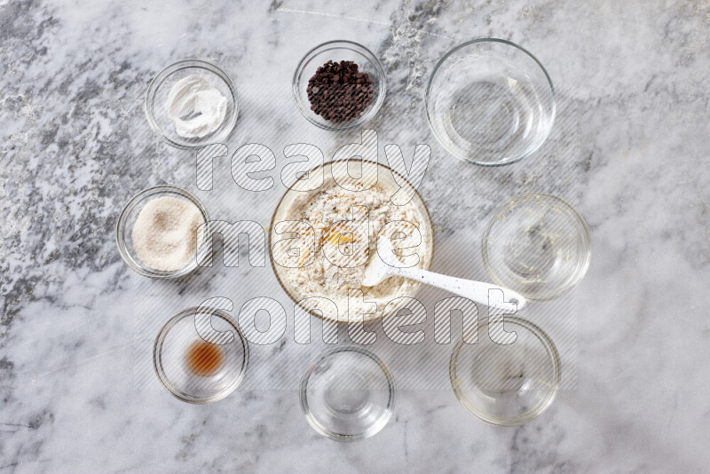 كوكيز خطوة بخطوة بمكوناتها، الدقيق، الزبدة، السكر البني، البيض، الفانيليا، السكر الأبيض، رقائق الشوكولاتة وصودا الخبز على خلفية رخام رمادي