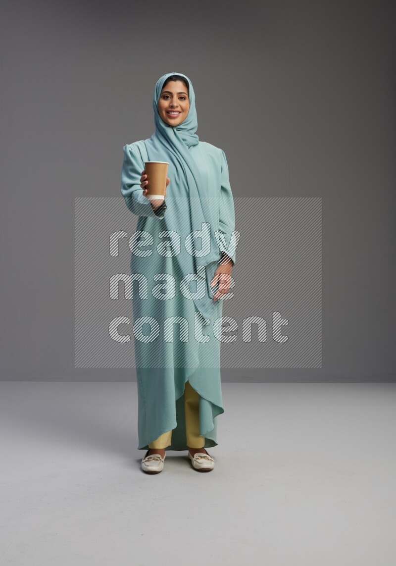 Saudi Woman wearing Abaya standing  holding paper cup on Gray background