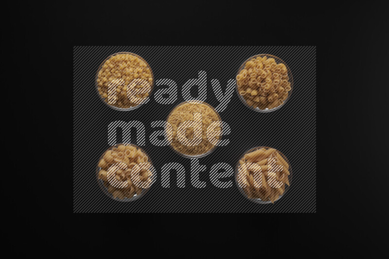 Different pasta types in 5 glass bowls on black background