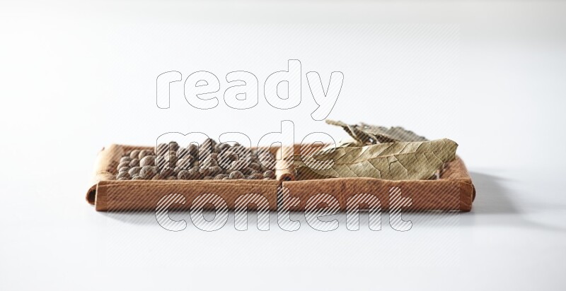 مربعان من أعواد القرفة ممتلئان ببهار الفلفل الحلو وأوراق الغار علي خلفية بيضاء