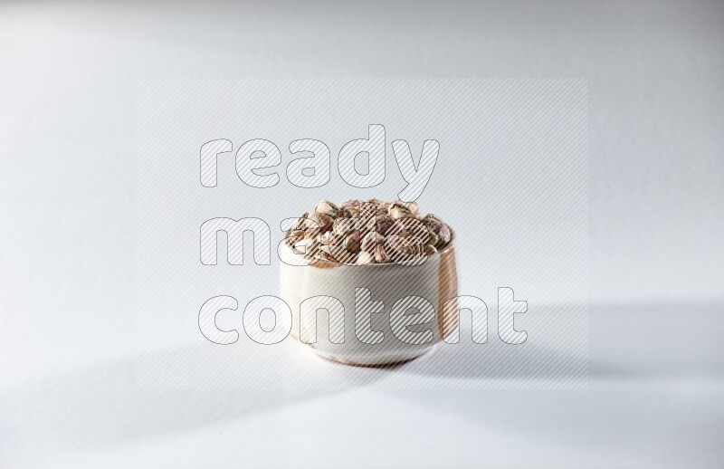 A beige ceramic bowl full of peeled pistachios on a white background in different angles