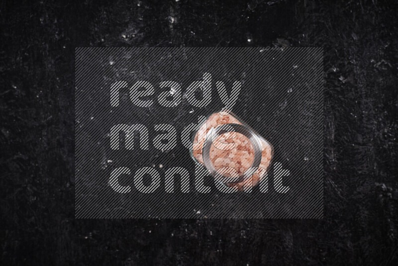 A glass jar full of coarse himalayan salt crystals on black background