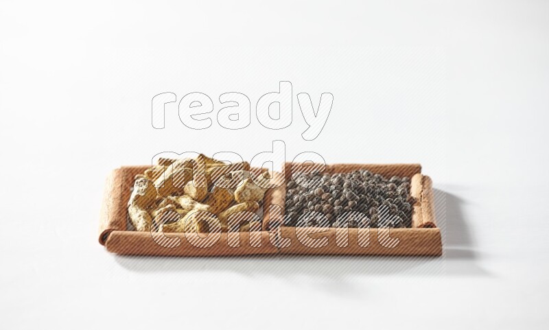 2 squares of cinnamon sticks full of black peppers and turmeric fingers on white flooring
