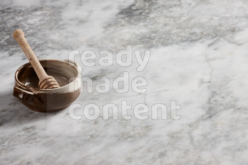 Multicolored pottery bowl with wooden honey dipper in it on grey marble background