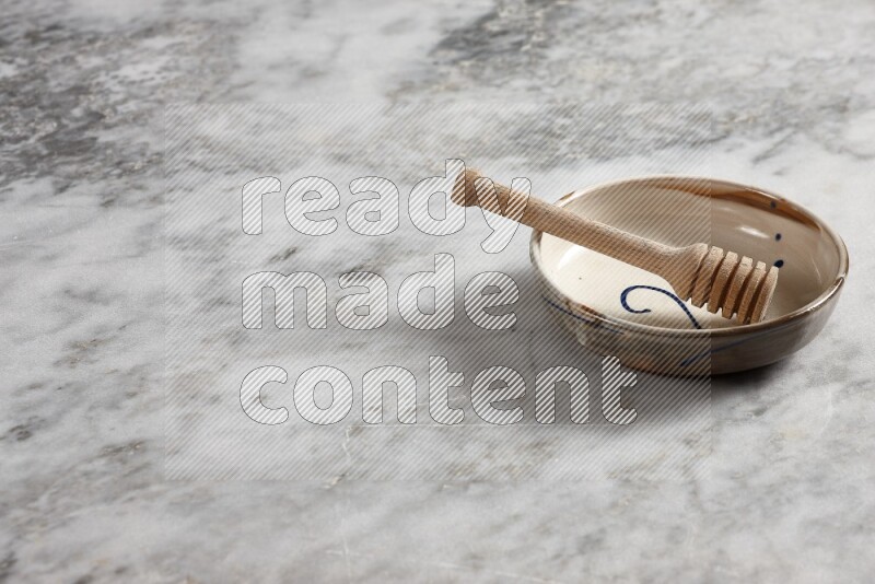 Multicolored pottery bowl with wooden honey dipper in it on grey marble background