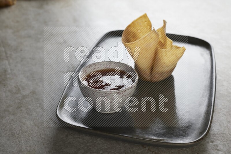 wonton cups with soy sauce ramkin on rectangle dark grey ceramic plate on grey textured counter top