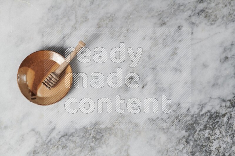 Multicolored pottery plate with wooden honey dipper in it on grey marble background