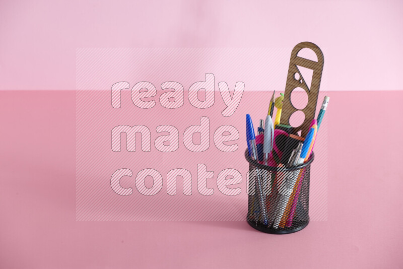 Pens, pencils and other different school supplies in a metal pen holder on rose background