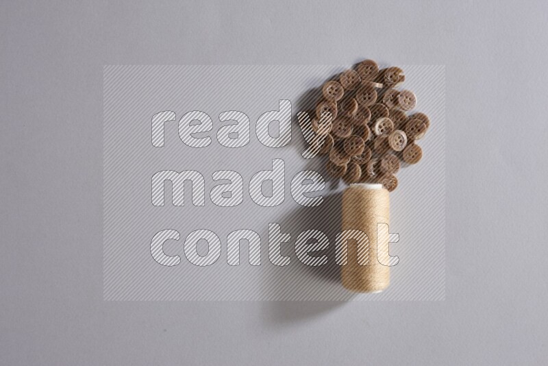 A beige sewing thread spool with colored buttons on grey background