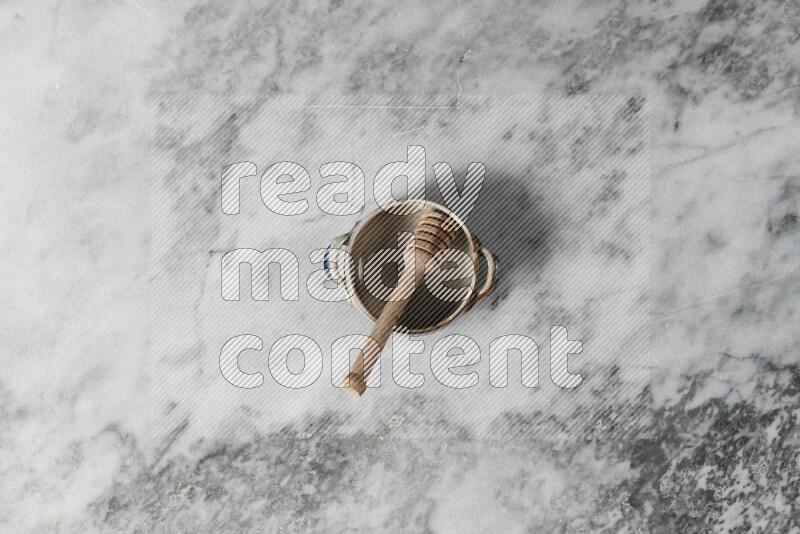 Multicolored pottery bowl with wooden honey dipper in it on grey marble background