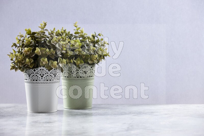Two different artificial plants in white and green decorative pots on grey marble background