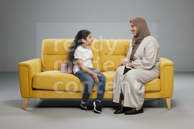 A girl sitting hiding a gift behind her back for her mother on gray background