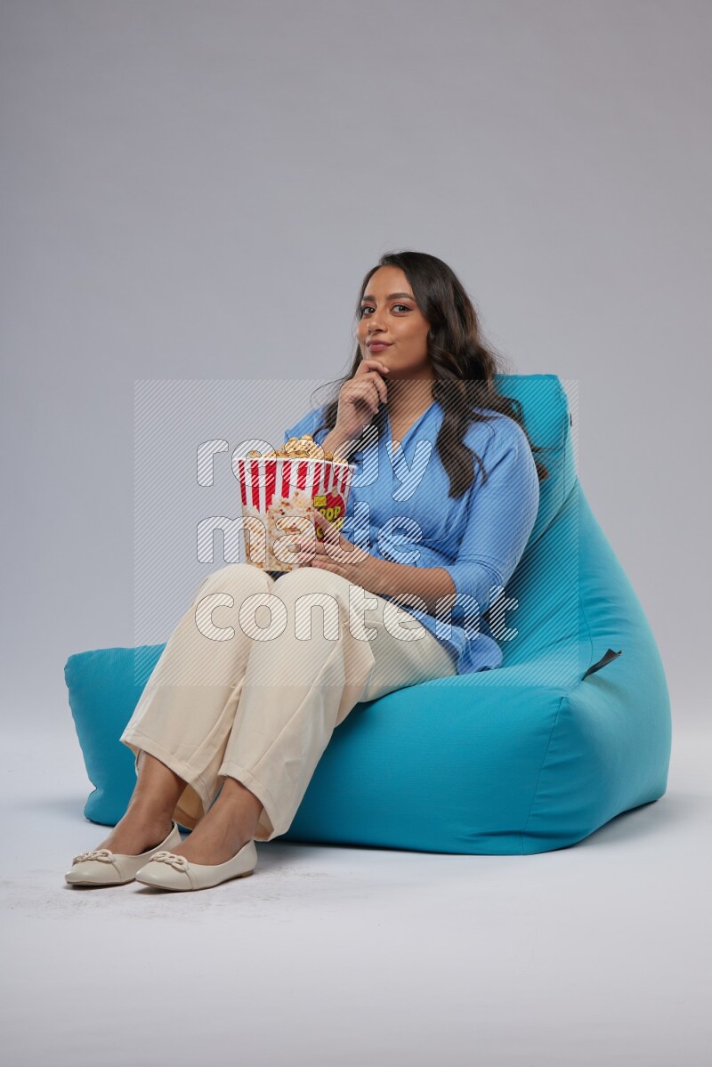 A woman sitting on a blue beanbag and eating popcorn