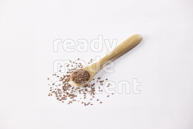 A wooden spoon full of flax seeds on a white flooring
