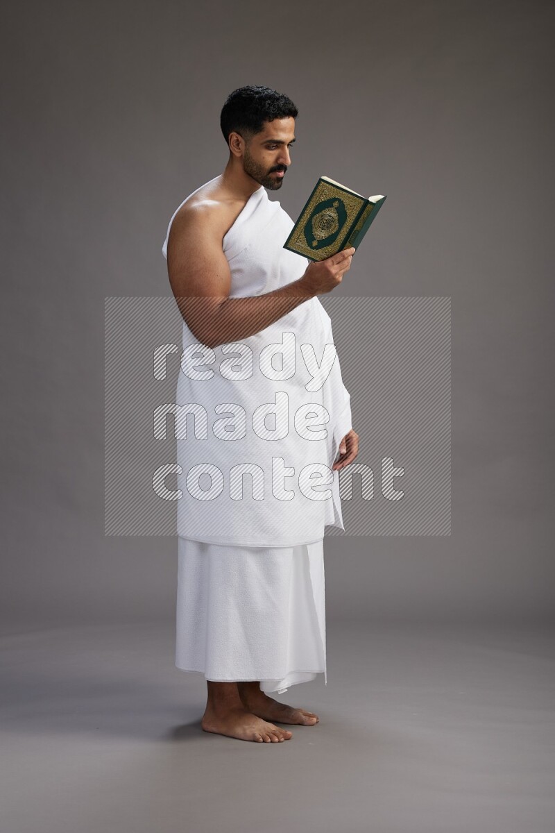 A man wearing Ehram Standing reading quran on gray background