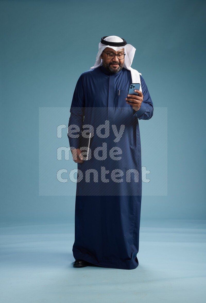 Saudi Man with shimag Standing texting on phone on blue background