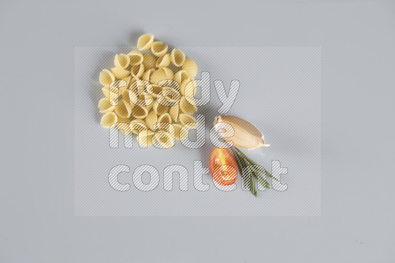 Raw pasta with different ingredients such as cherry tomatoes, garlic, onions, red chilis, black pepper, white pepper, bay laurel leaves, rosemary, cardamom and mushrooms on light blue background