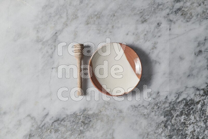 Multicolored pottery plate with wooden honey dipper on the side on grey marble background