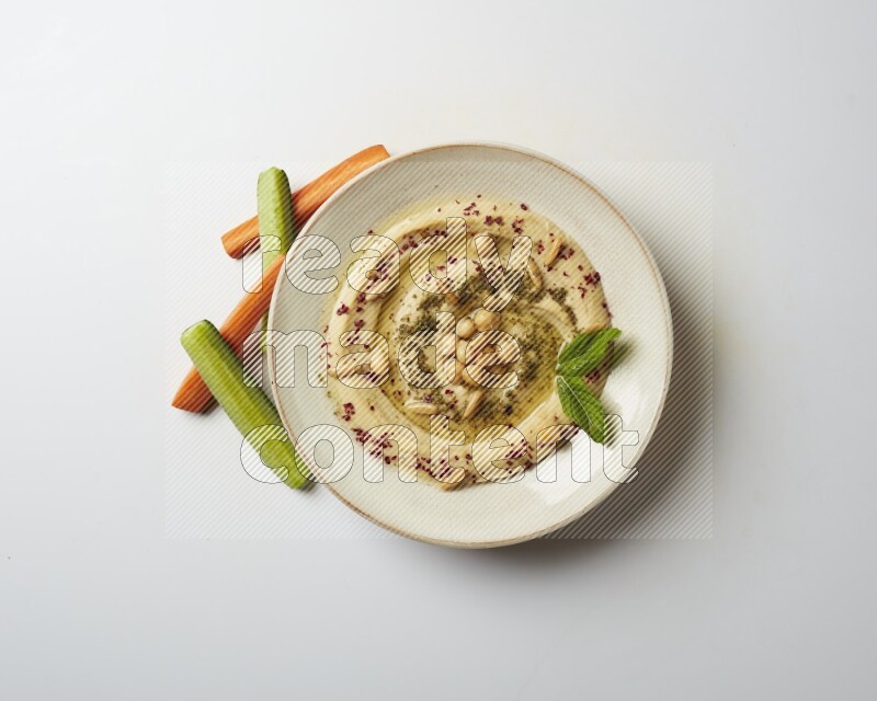 Hummus in a pottry plate garnished with zaatr & sumak on a white background