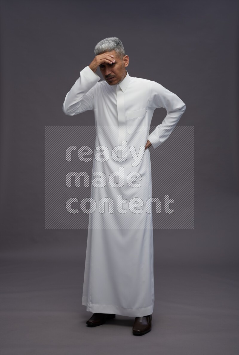 Saudi man wearing thob standing interacting with the camera on gray background
