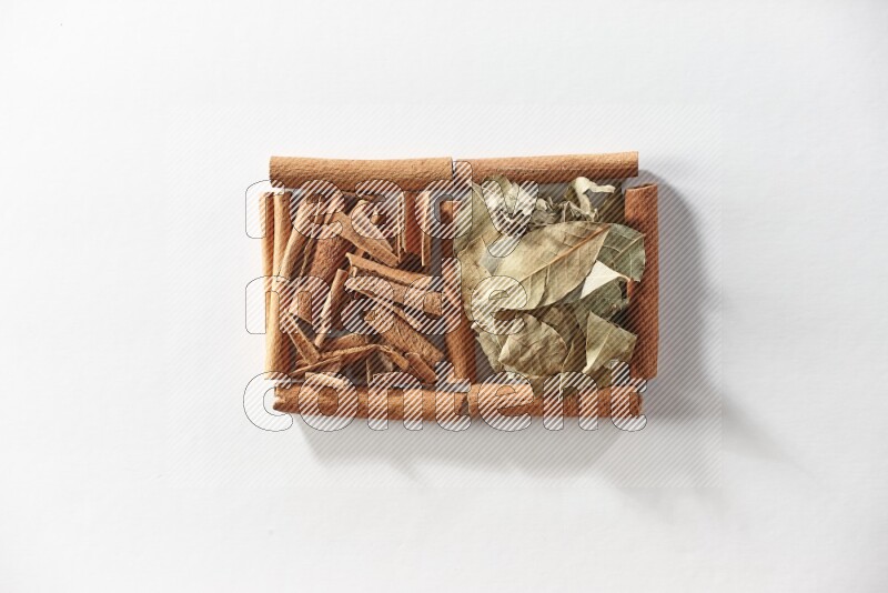 مربعان من أعواد القرفة ممتلئان بقطع من القرفة وأوراق الغار علي خلفية بيضاء