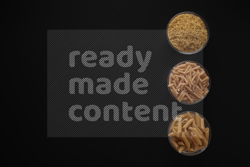 Different pasta types in 3 glass bowls on black background
