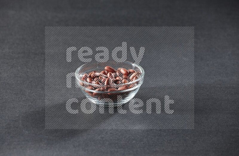 A glass bowl full of red skin peanuts on a black background in different angles