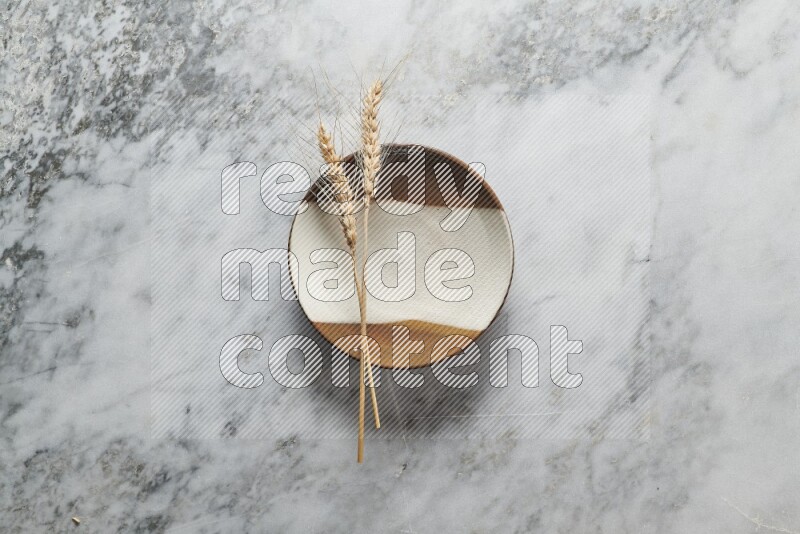 Wheat stalks on multicolored pottery plate on grey marble background