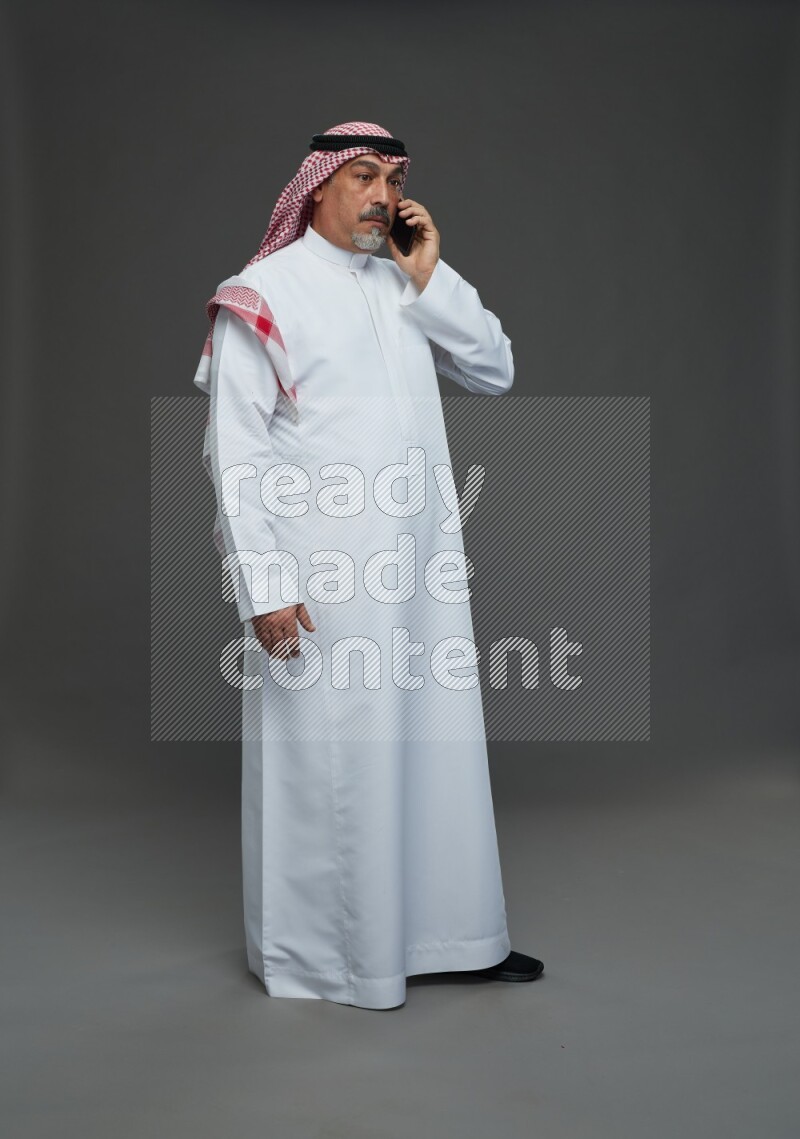 Saudi man with shomag Standing talking on phone on gray background